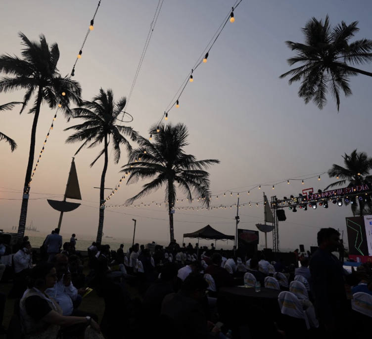 The sun going down over the Arabian Sea behind the stage, with string lights and palms above the seated room